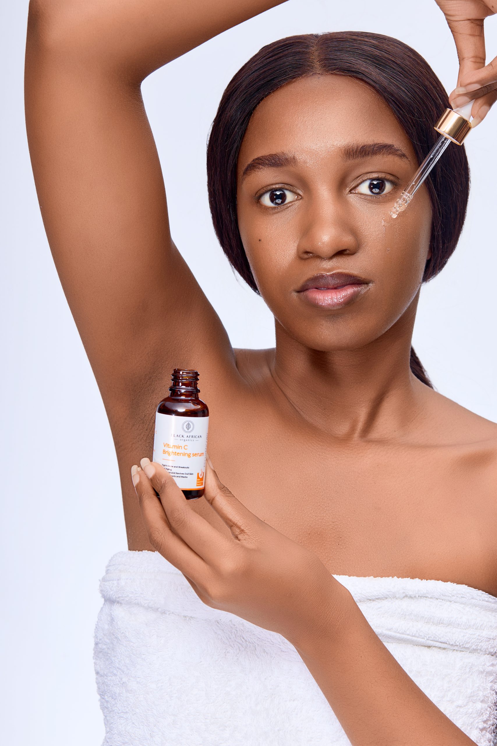 Woman holding a dropper bottle of serum while applying it under her arm.